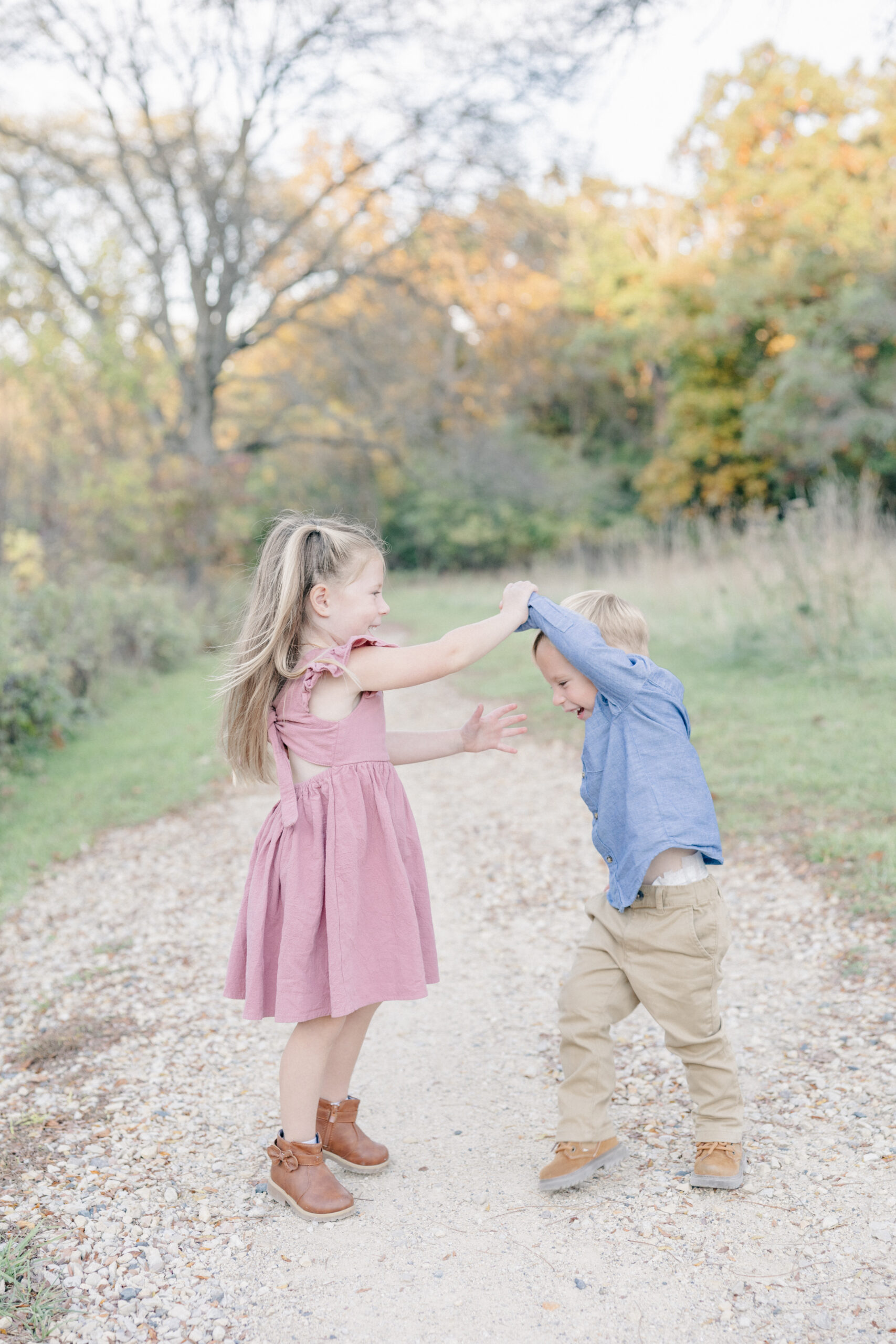 Toddler girl twirls toddler boy in forest preserve.