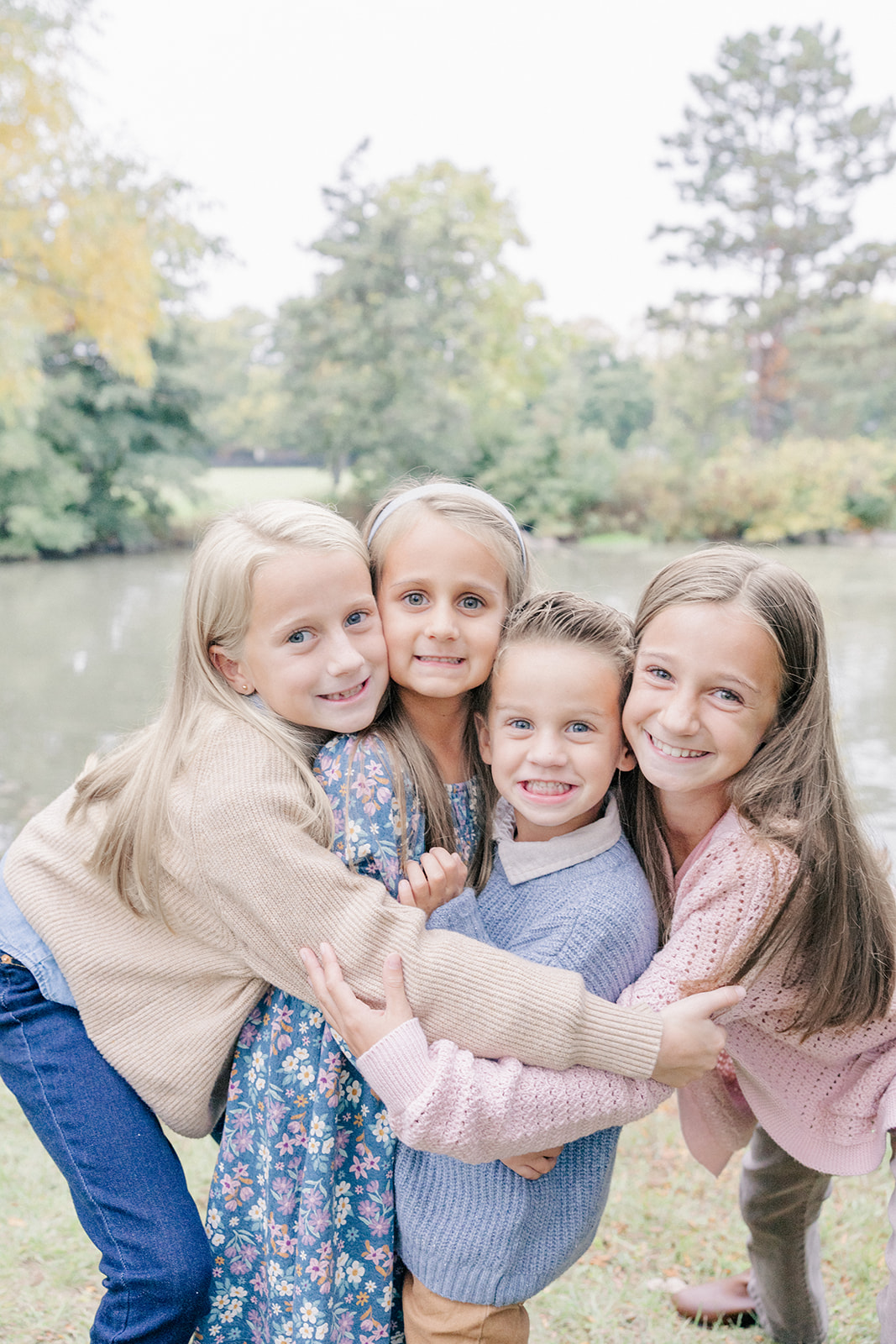 three young girls lovingly hug young boy in an outdoor family photography session