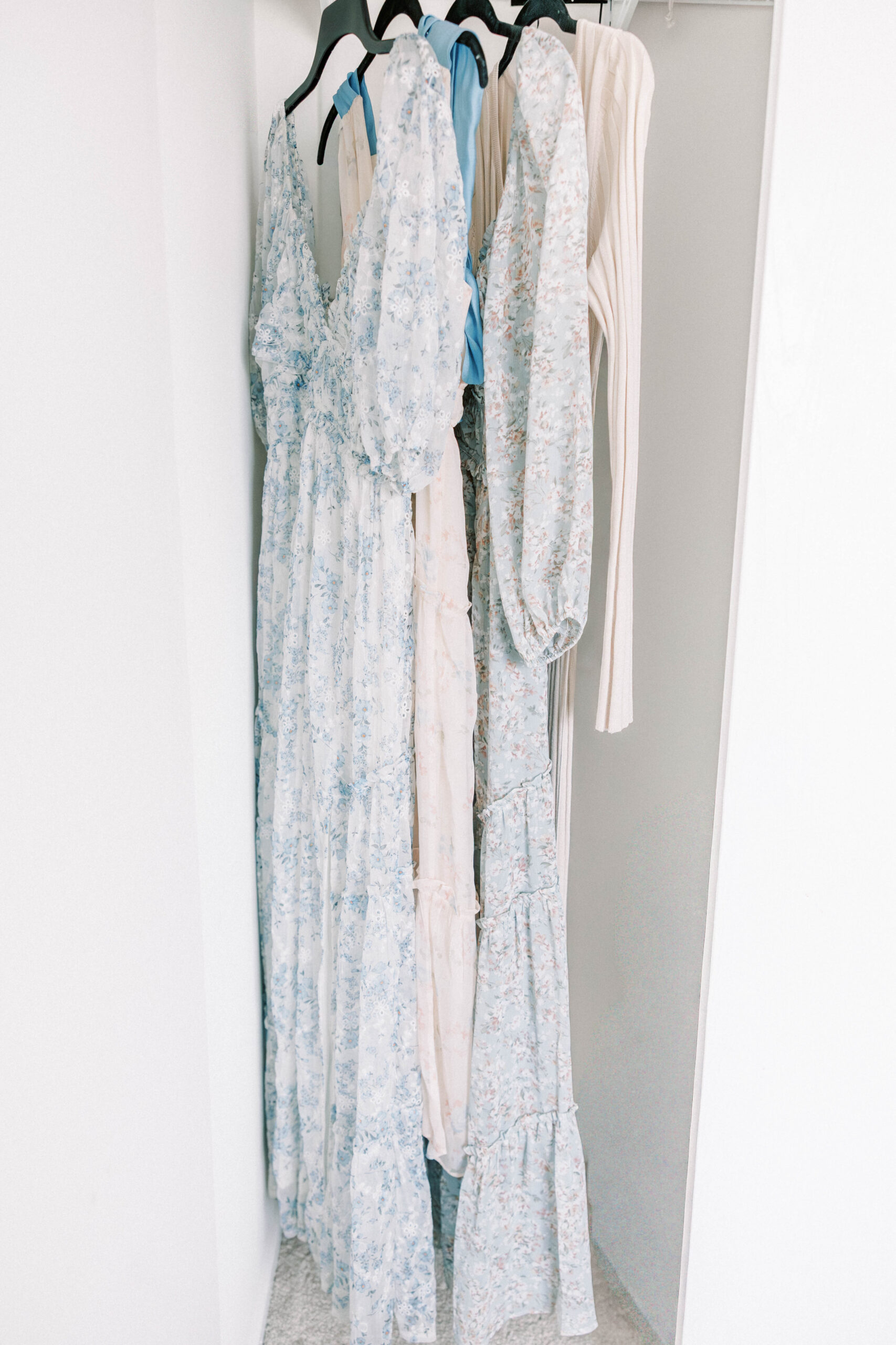 Four long neutral colored dresses flow as they hang in a natural light room.