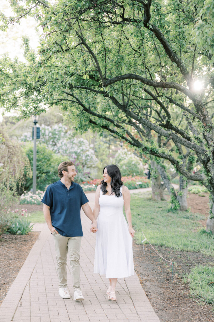 Man and woman walk along nature pathway holding hands.